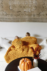Two kids peeking out from under a Nuzzie blanket on the couch. #Color_Marigold