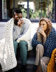 Young man and woman sitting outside with Nuzzie blankets drinking coffee #Color_Cream
