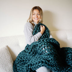 Woman cuddling Nuzzie knit weighted blanket on couch #Color_Forest-Green