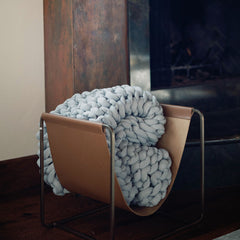 Rolled Nuzzie blanket next to fireplace. #Color_Misty-Grey